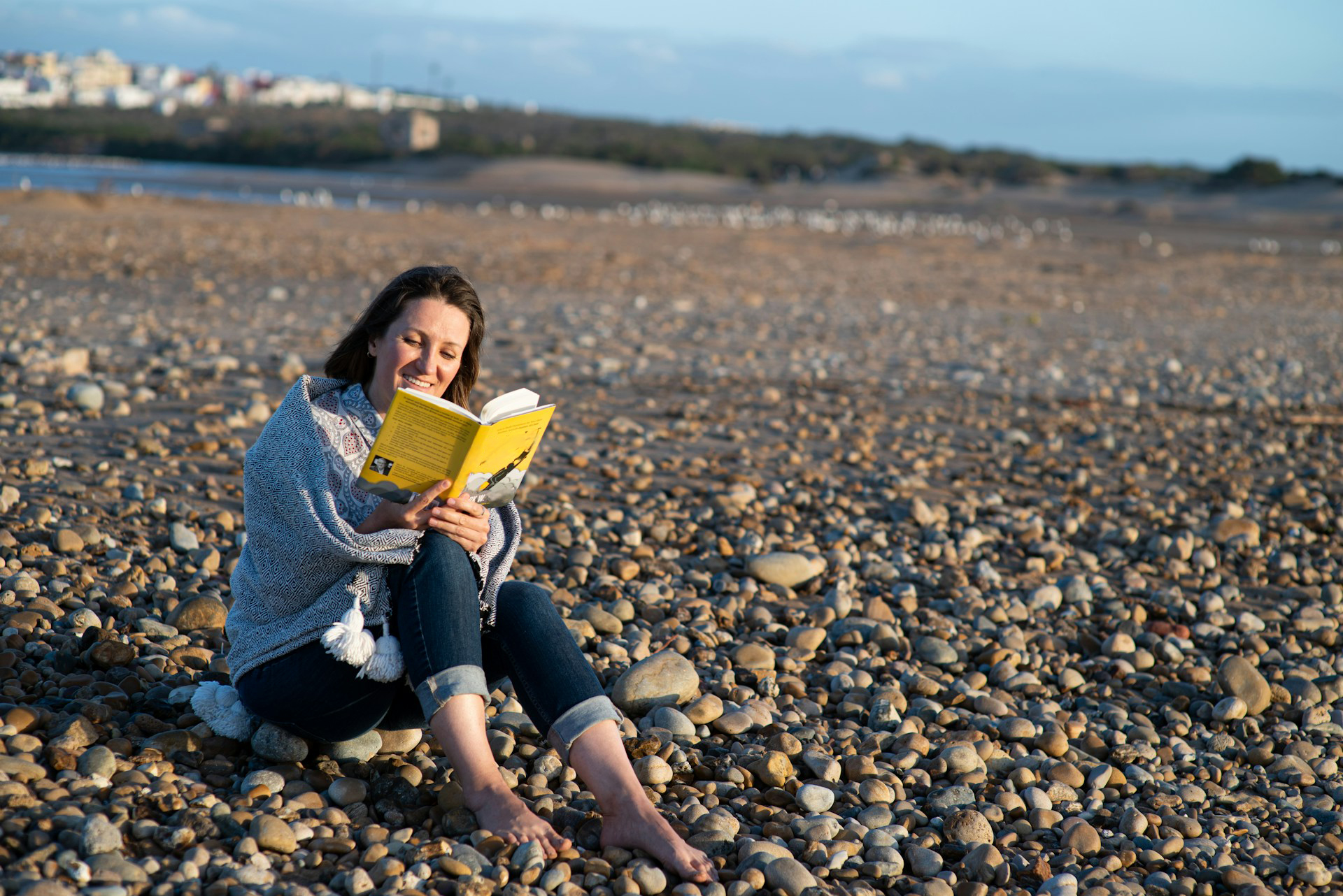 Image shows woman reading a book on the beach to illustrate the idea of choosing a book signing location.
