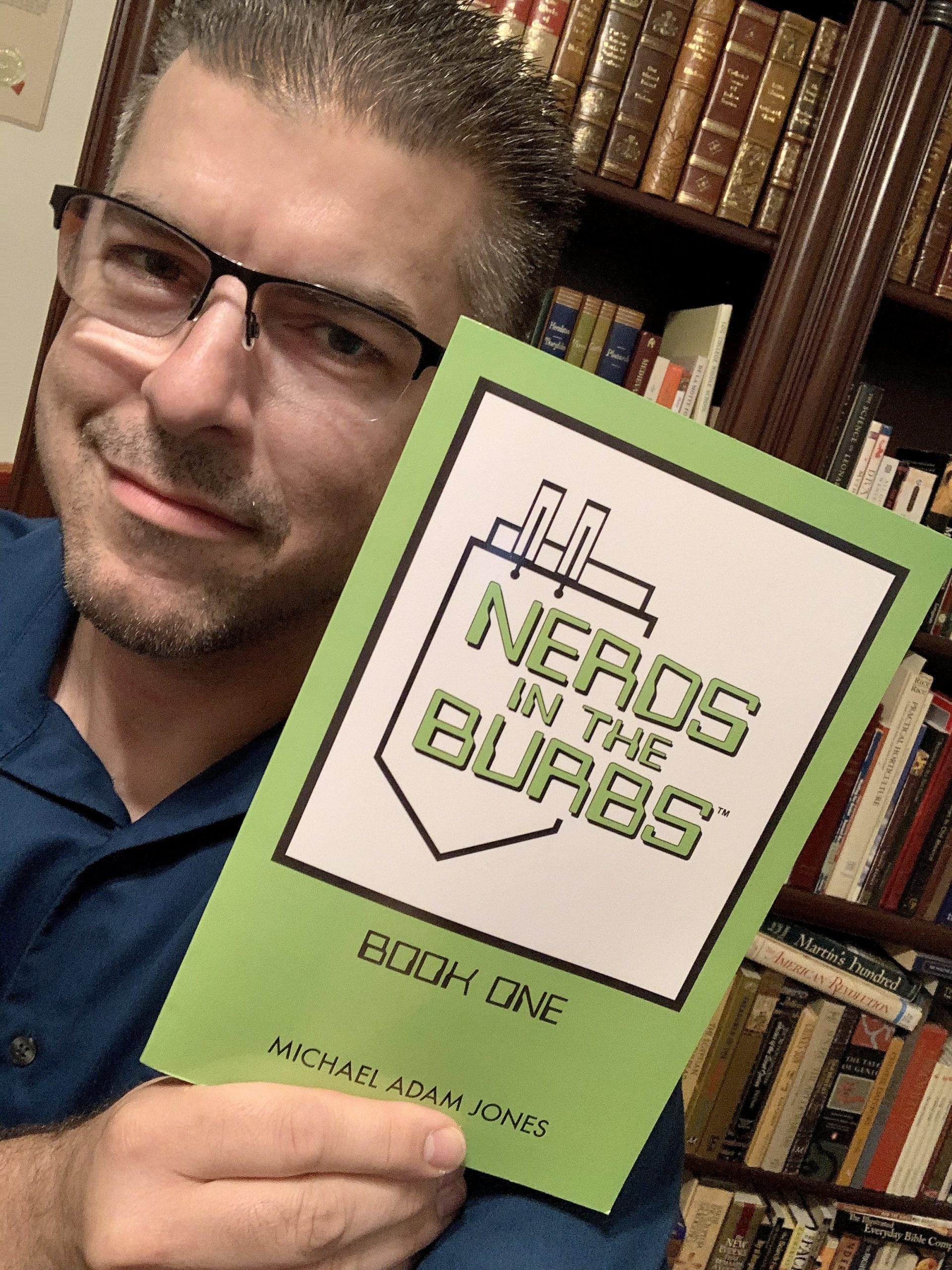 Image shows author-illustrator Michael Adams Jones holding his book, Nerds in the Burbs.