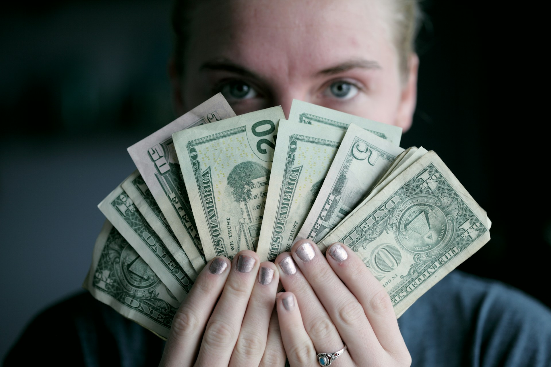 Image shows a person holding cash in front of her face to illustrate the article topic: How much does it cost to self-publish a novel?